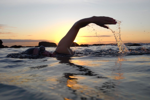 a person swims in an ocean pool at sunrise
