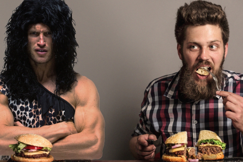 Caveman dressed in animal skins eats burger with modern human man