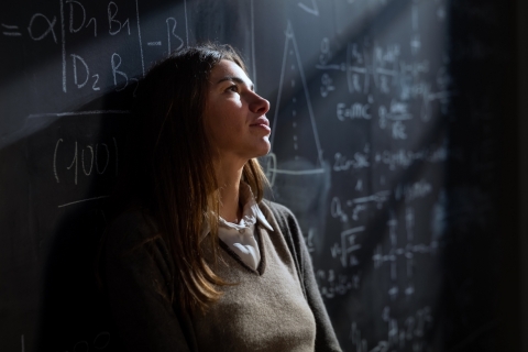 cinematic shot of young teacher leaning against blackboard