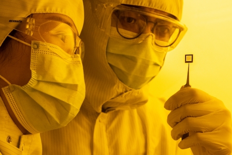 researchers in lab coats and masks analysing an array of  transistors