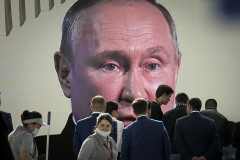 vladimir putins face on a large screen behind people in the street