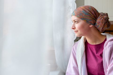 young adult female cancer patient wearing headscarf looking out window
