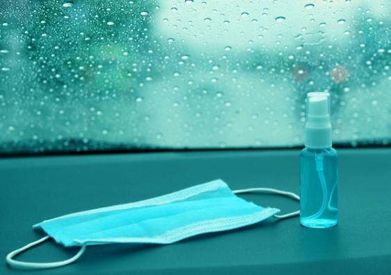 A face mask and bottle of hand sanitiser next to a rainy window