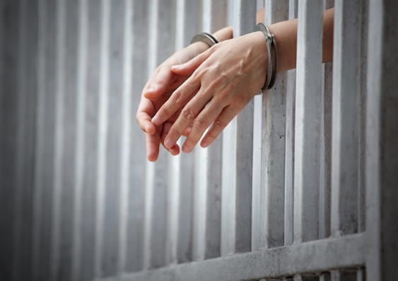 A pair of handcuffed hands poking through bars of a jail cell