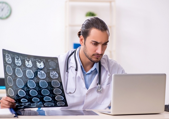 Doctor examines computer while holding scans of patient's brain