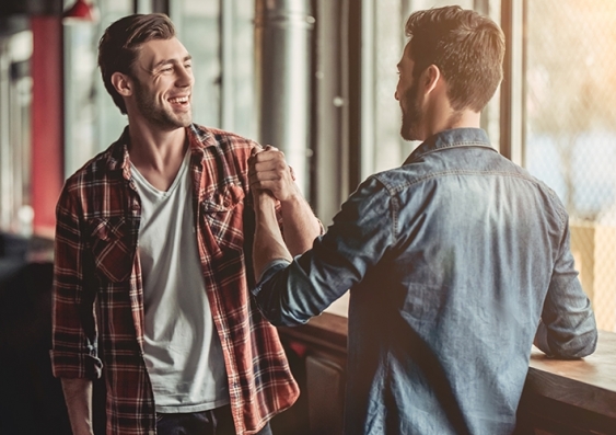 Two smiling young men dressed casually do a left-arm 'bro handshake'