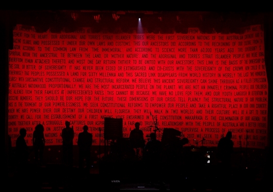 Silhouettes of a rock band with text from the Uluru Statement of The Heart in the background