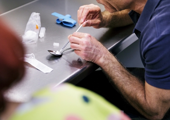 A man prepares to draw injection drugs into a syringe while someone watches