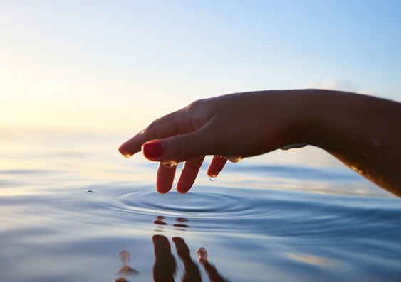 A hand is held just above rippling water