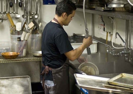 A kitchen worker cleans cooking utensils
