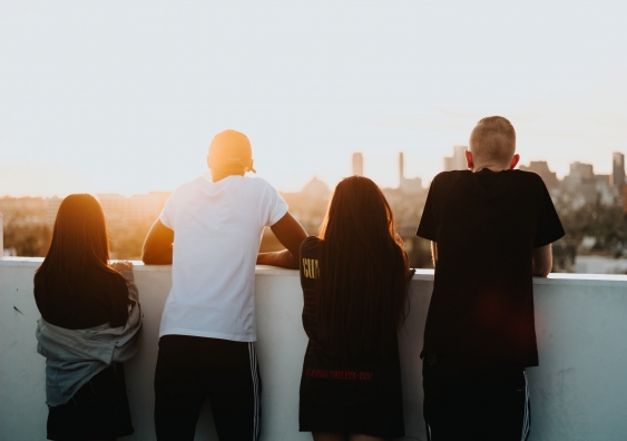 4 young people on a balcony looking at a sunset over the city