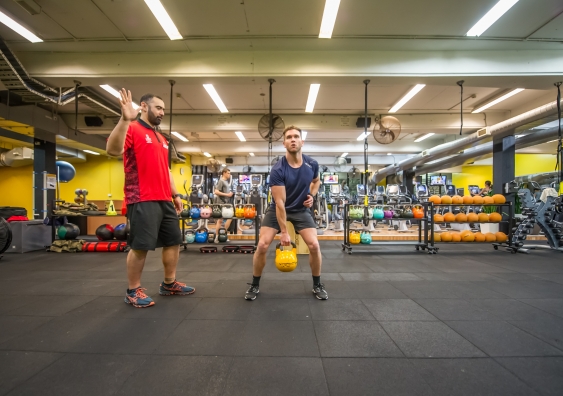 A trainer directing a man lifting a kettlebell