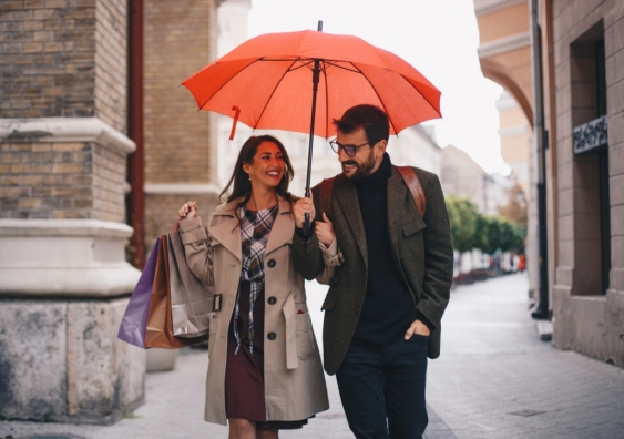 Man and woman holding shopping bags walk under an umbrella
