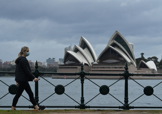 a masked woman walks by sydney opera house