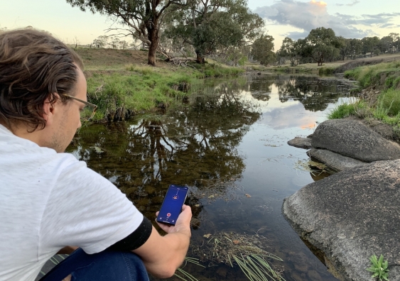 a person holding a smartphone using the frogid app near a body of water