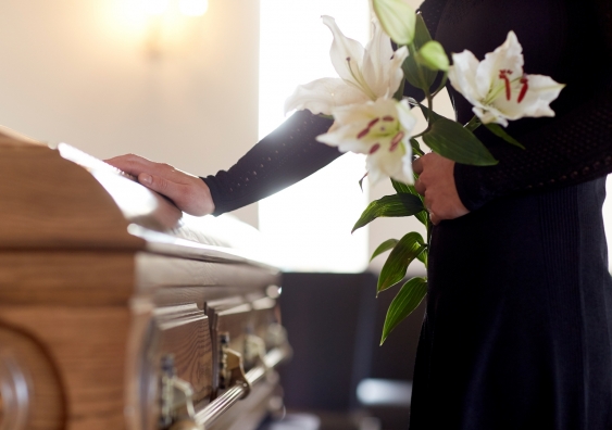 a person in mourning puts a hand on a coffin at a funeral