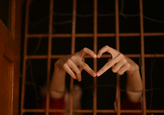 A person reaching through bars with a hand gesture of a love heart