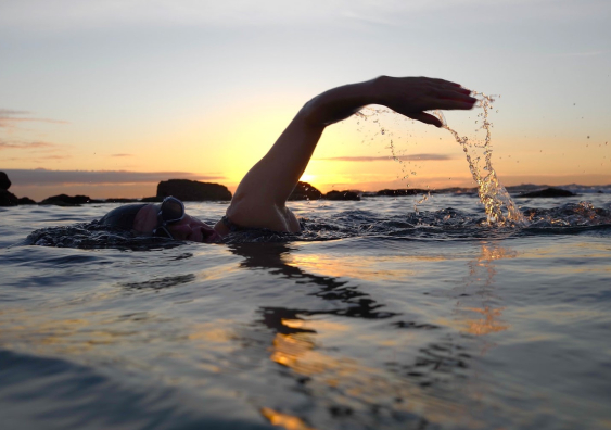a person swims in an ocean pool at sunrise