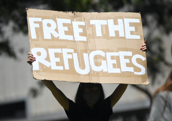 a street protester holds a sign that says free the refugees