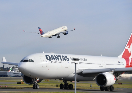 a qantas plane taxis on the tarmac with a delta flight taking off behind it