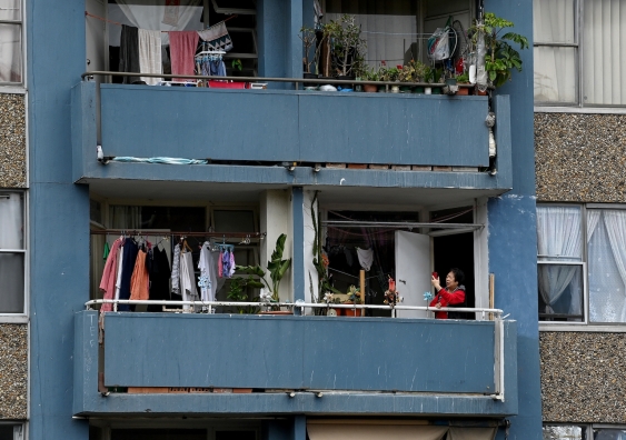 a woman stands on an apartment balcony crowded with clothes lines