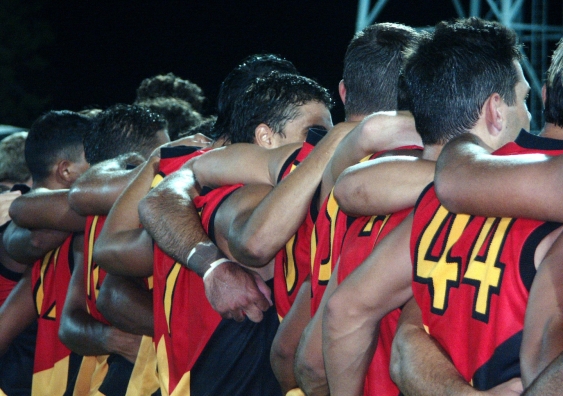aboriginal football players stand with their arms around each others shoulders