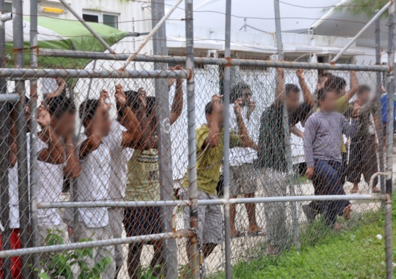 asylum seekers look through a wire fence at a detention centre