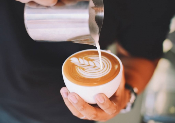 Barista pours latte art into cup of coffee