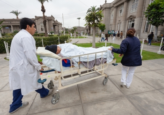 Healthcare workers transport a patient on a hospital bed between hospital buildings.