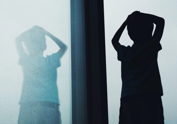 A silhouette of  a child standing by a window with a reflection