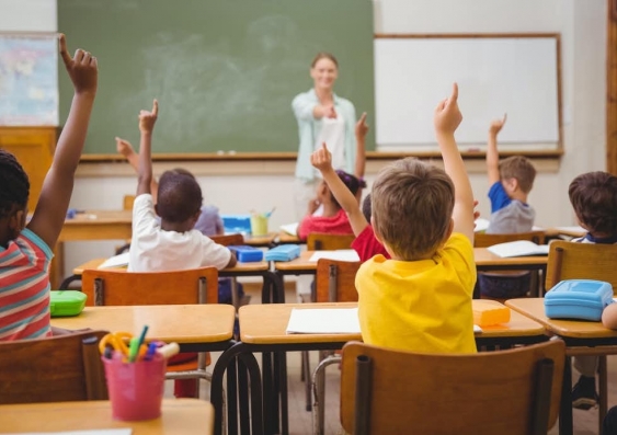 Children sit in a classroom, raising their hands