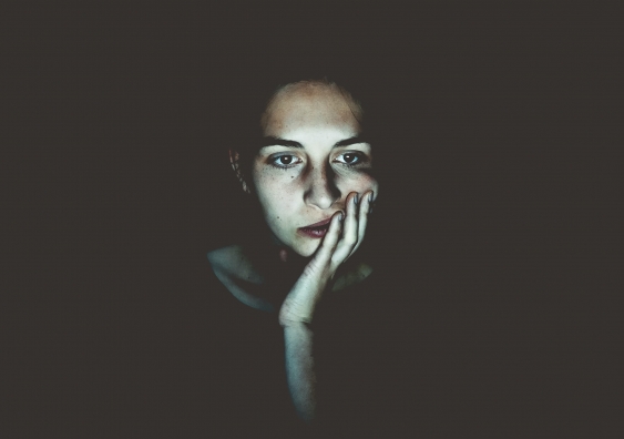 A woman in a dark room with her hand on her cheek, her face lit by a screen