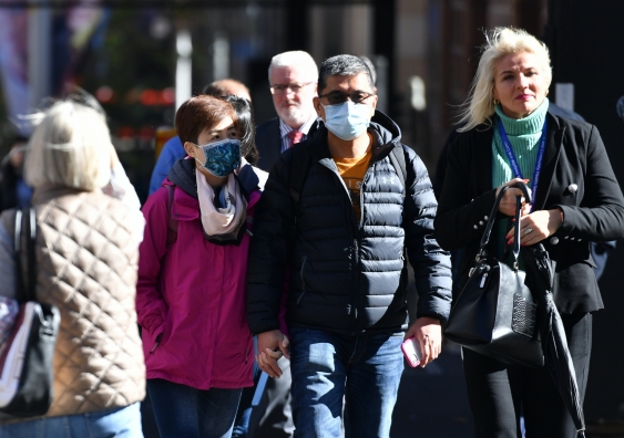 Two people wearing masks on the street next to a woman without a mask
