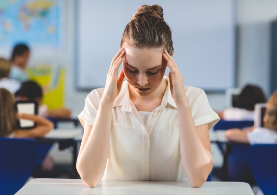 depressed female teacher touching her head in classroom