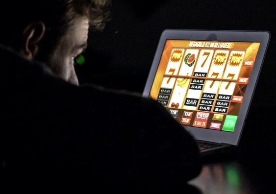 a man stares at a gambling game on a screen in a dark room