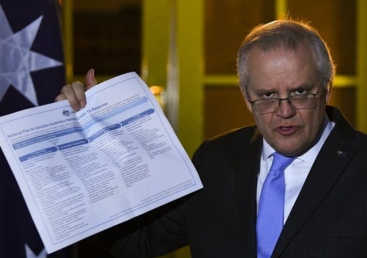 Prime Minster Scott Morrison holds up the National COVID-19 Plan at a press conference