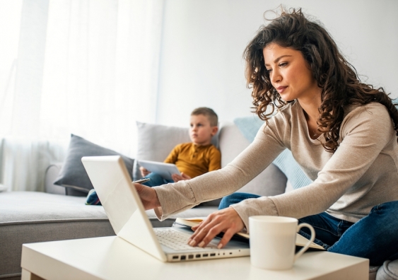 woman working on laptop sitting on sofa with child next to her
