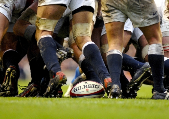 rugby players' legs during a game, with rugby ball in the photo's centre