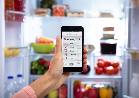 person holding a smartphone with a shopping list on screen in front of an open fridge