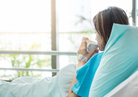 woman in hospital bed sipping from a mug