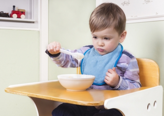 A child in a high chair plays with a bowl of food