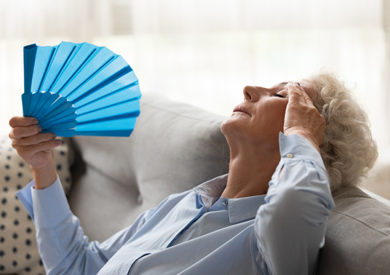 An elderly woman looking uncomfortable fans herself