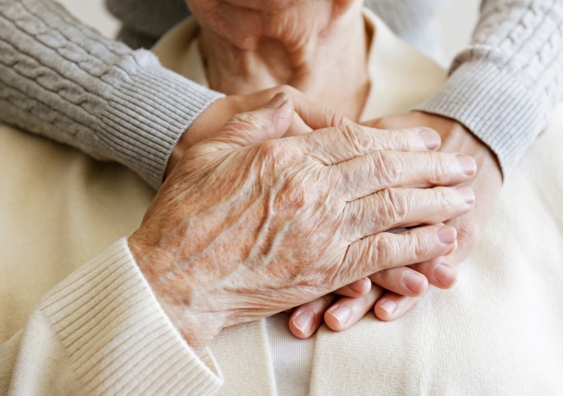 Elderly woman places hand over younger woman's hands who hugs her from behind