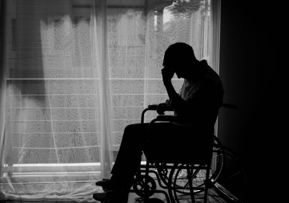 Silhouette of person sitting on wheelchair in front of a window