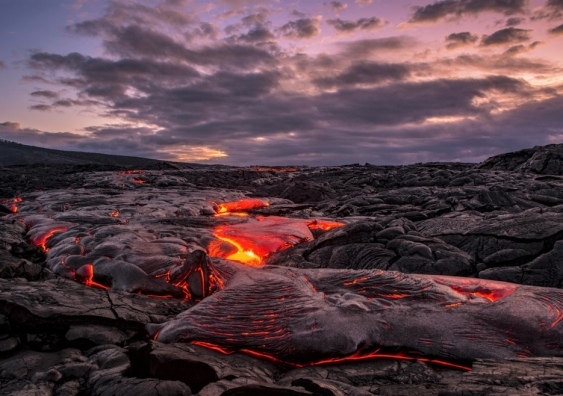 Lava flowing over rocks under a cloudy dawn sky