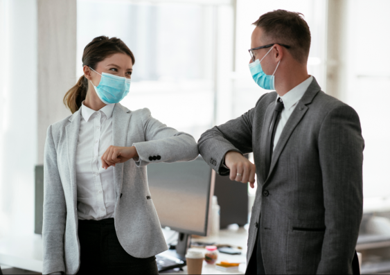 Two people in the workplace with masks on knocking elbows in greeting.