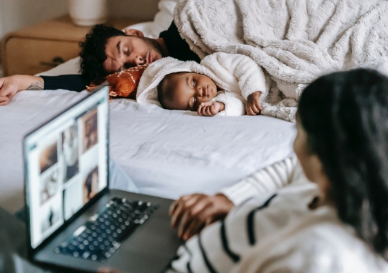 Woman working on laptop looks over at partner and baby sleeping