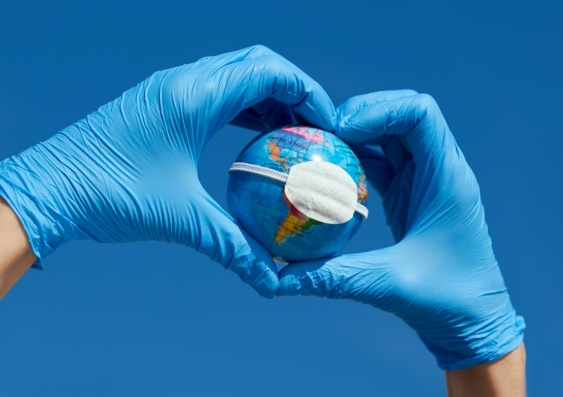 planet earth with a facemask being held by a human hands with surgical gloves