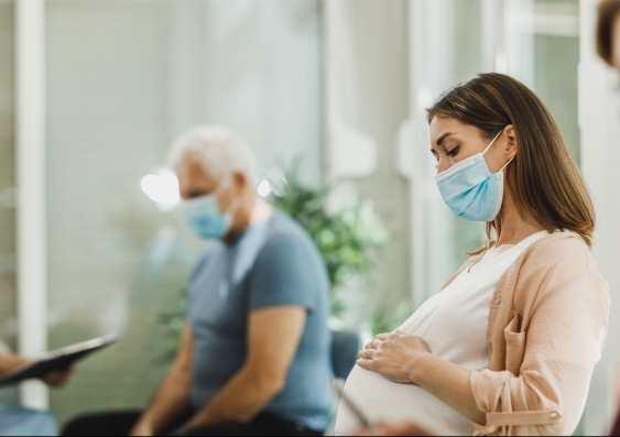 Pregnant person in a waiting room wearing a mask
