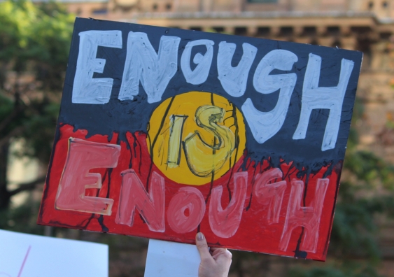 A sign is held in the air at a protest, stating: Enough is Enough